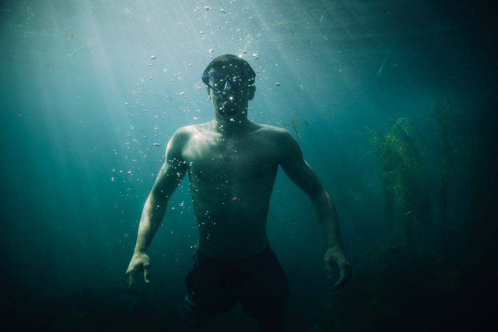 Nageur sous l'eau regardant l'objectif, le soleil perçant la surface