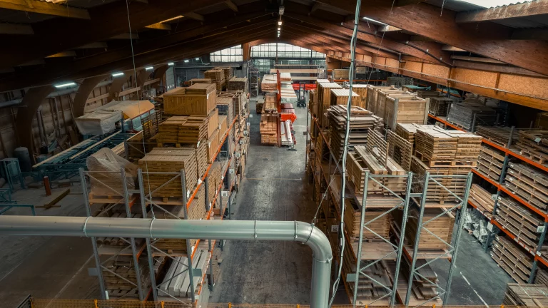 Reportage m&eacute;tier : entrep&ocirc;t de bois film&eacute; en hauteur, rayonnages charg&eacute;s de palettes