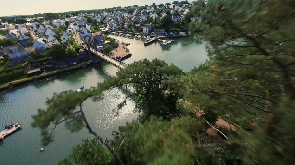 Vol de drone FPV au ras des pins, au-dessus d&rsquo;un port bord&eacute; de maisons
