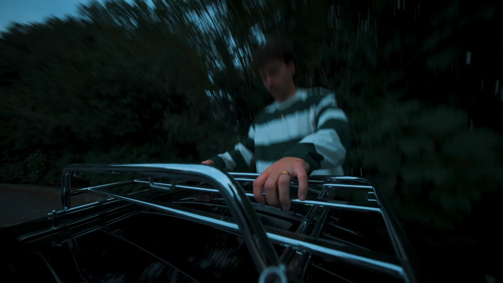 Jeune homme posant la main sur le porte-bagages chrom&eacute; d'une Mazda MX-5, en lisi&egrave;re de for&ecirc;t au cr&eacute;puscule